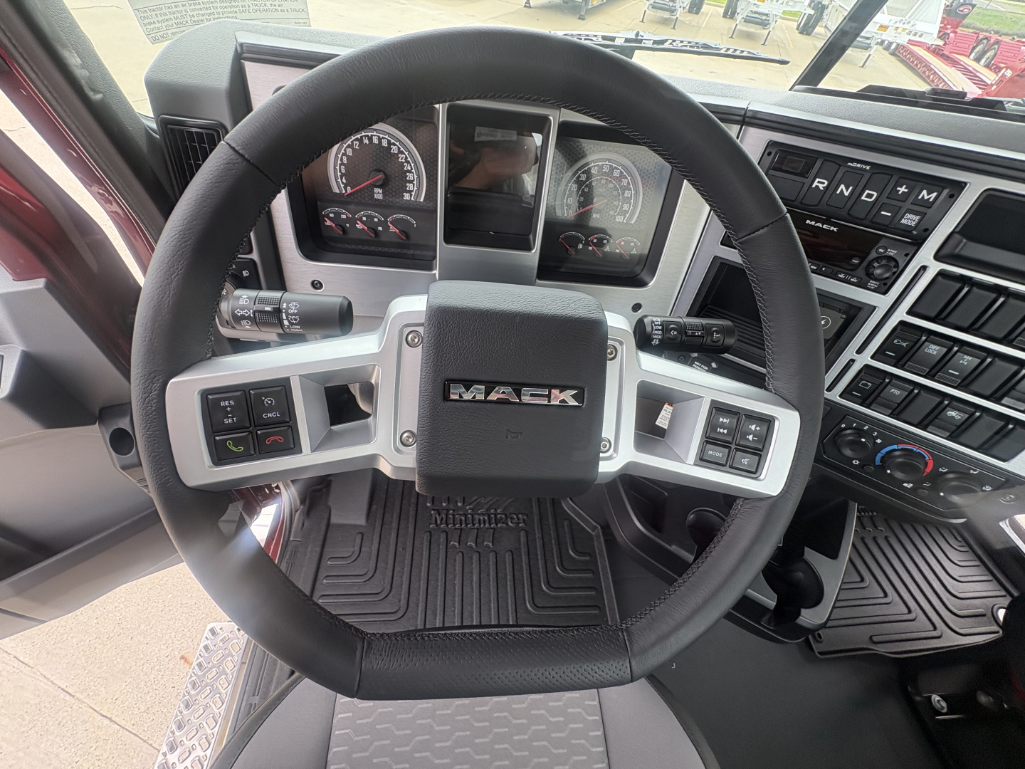 Steering wheel and dashboard of a Mack PI64T truck cab showing instrument cluster and controls.