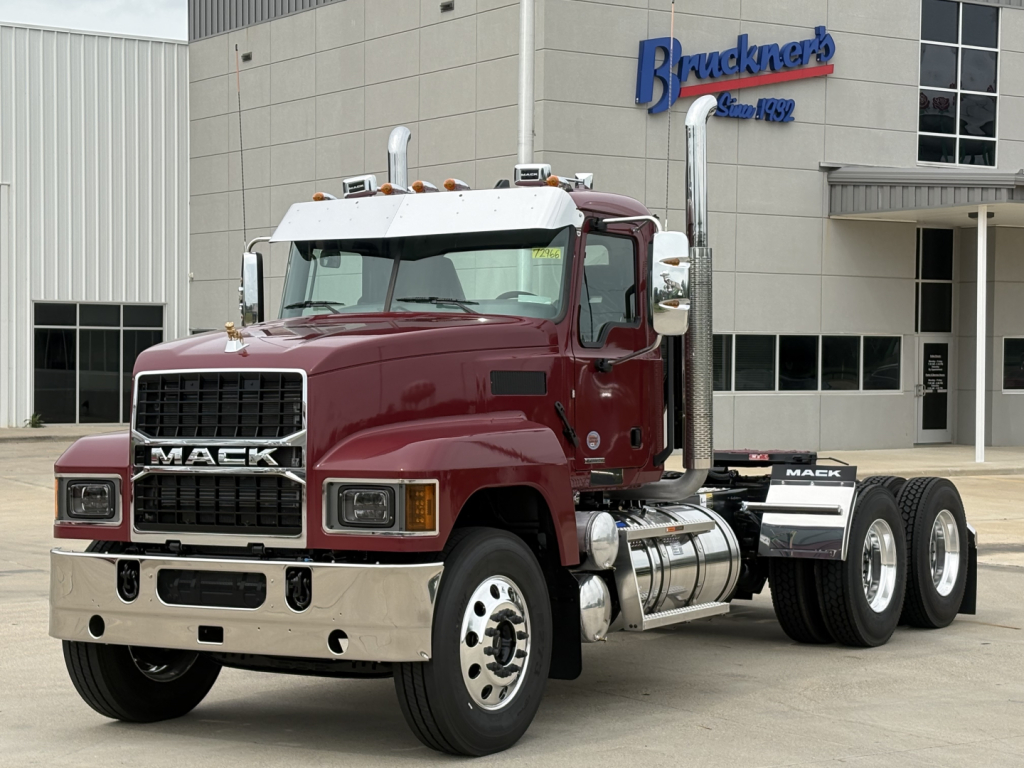 Mack PI64T conventional daycab truck in burgundy with chrome bumper and dual exhaust stacks parked in front of a dealer building.
