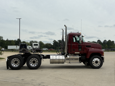 Truck chassis of a 2027 Mack PI64T with maroon cab and dual rear axles, side view showing fuel tanks and exhaust stacks.