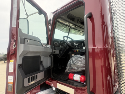 Truck cab interior showing Mack PI64T dashboard and steering wheel with exposed driver's door open.