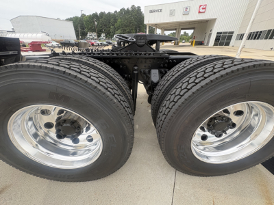 Twin rear axles of a Mack PI64T truck showing dual wheels and suspension components; chrome rims; chassis cab in background with service building.