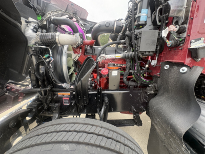 Mack PI64T engine bay showing front suspension, hoses, wiring, and coolant reservoir with various components visible.
