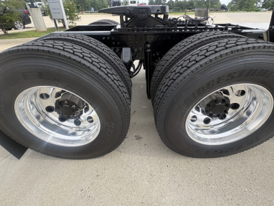Twin rear truck axles with Bridgestone tires and polished chrome rims, chassis framing visible between wheels under a Mack PI64T tractor.