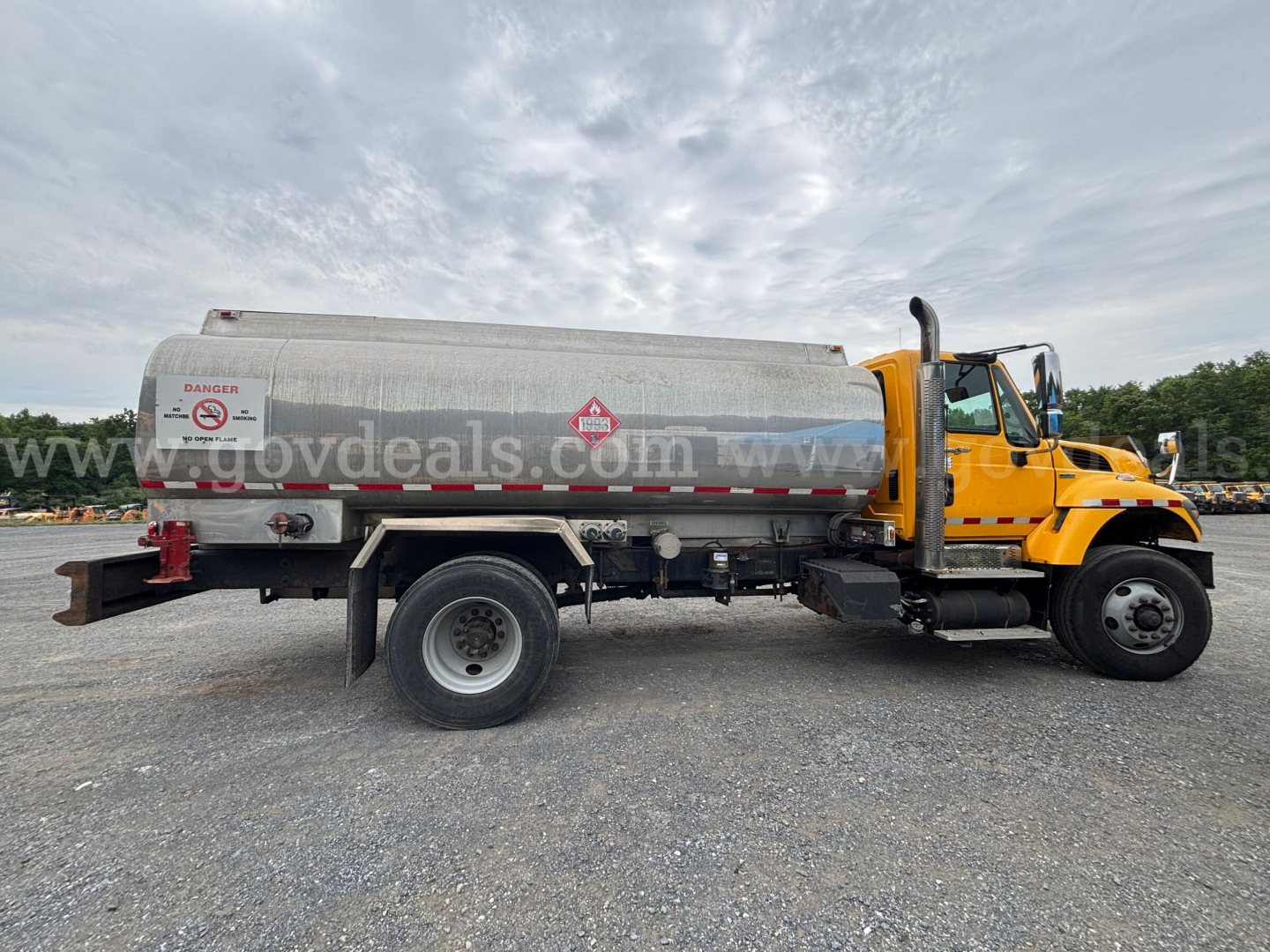 Tank truck side view showing cylindrical stainless tank with hazard placards and yellow cab, International 7400 used vehicle
