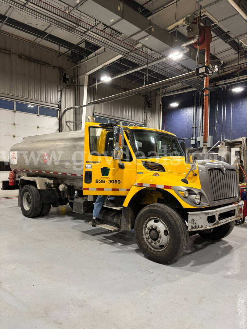 Tank truck in a yellow cab inside a workshop. Visible text includes 836 3069 on door, and tank with faint watermark-like text. Ceiling utilities and equipment overhead.
