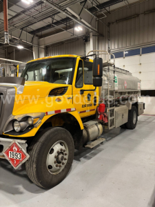 2008 International 7400 water tanker truck in a warehouse with yellow cab and silver tank; front bumper, headlights, and warning placard visible; stock number plate and VIN text not legible.