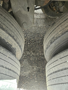 Dual axles with tires and gap between wheels in a trailer chassis showing ground surface.