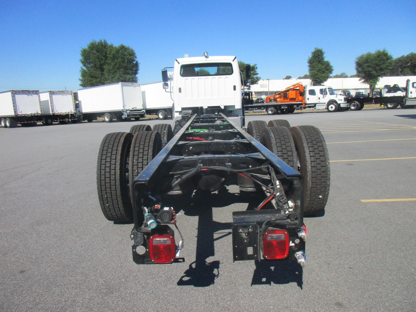 Chassis rear view showing frame rails, dual rear wheels, and taillights on Freightliner Business Class M2 106 Plus cab and chassis; clear blue sky.