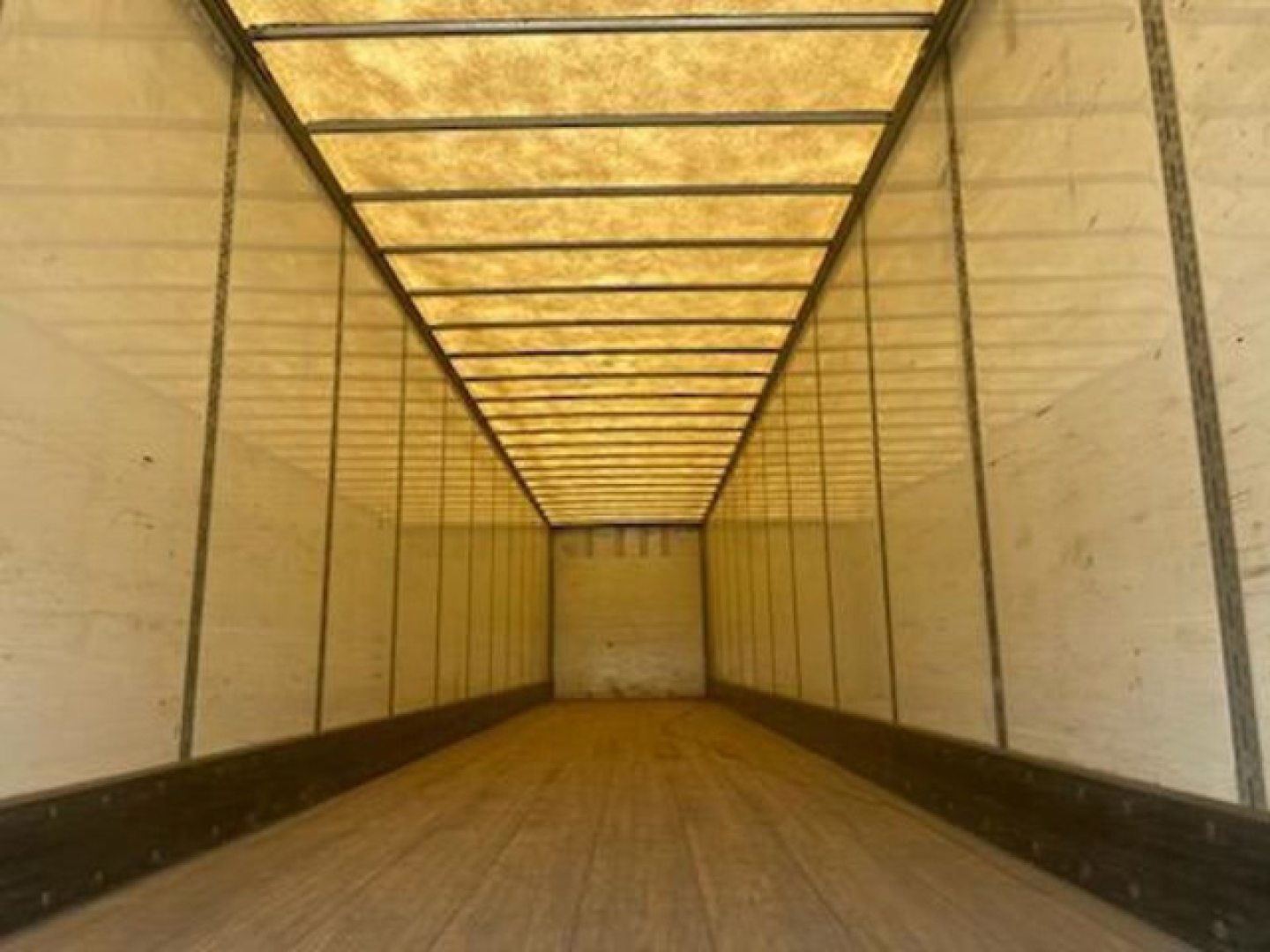 Trailer interior showing empty cargo area with wooden floor, white sidewalls, and overhead lighting rails.