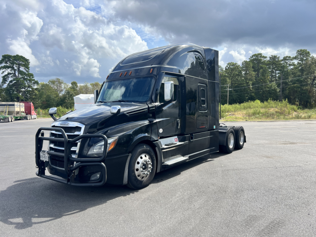 Freightliner heavy-duty tractor-trailer in a parking lot showing a black exterior, aerodynamic cab, front bull bar, chrome accents, and dual rear axles.