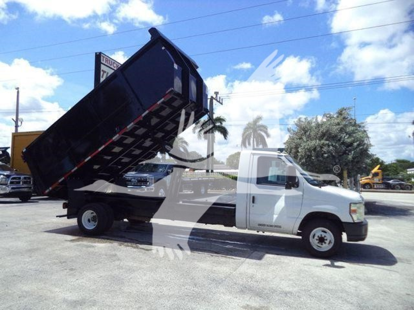 Ford E450 dump truck showing raised black dump bed attached to white cab