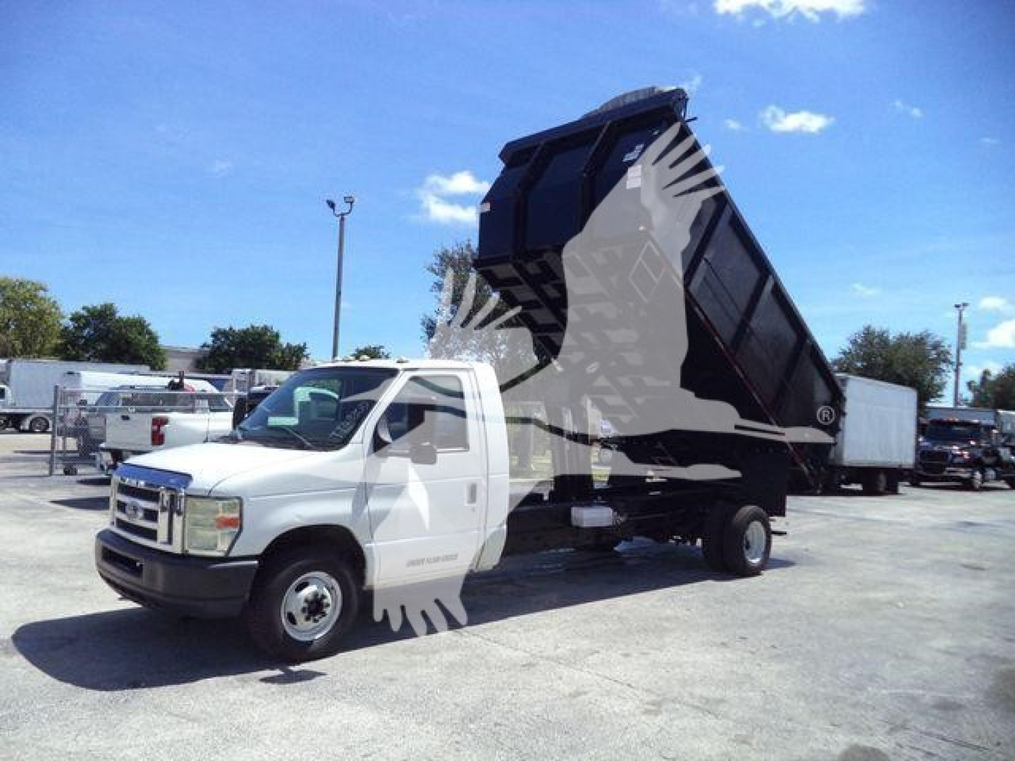 Ford E-450 dump truck with raised bed in a parking lot, white cab and black dump body, stock image with watermark.