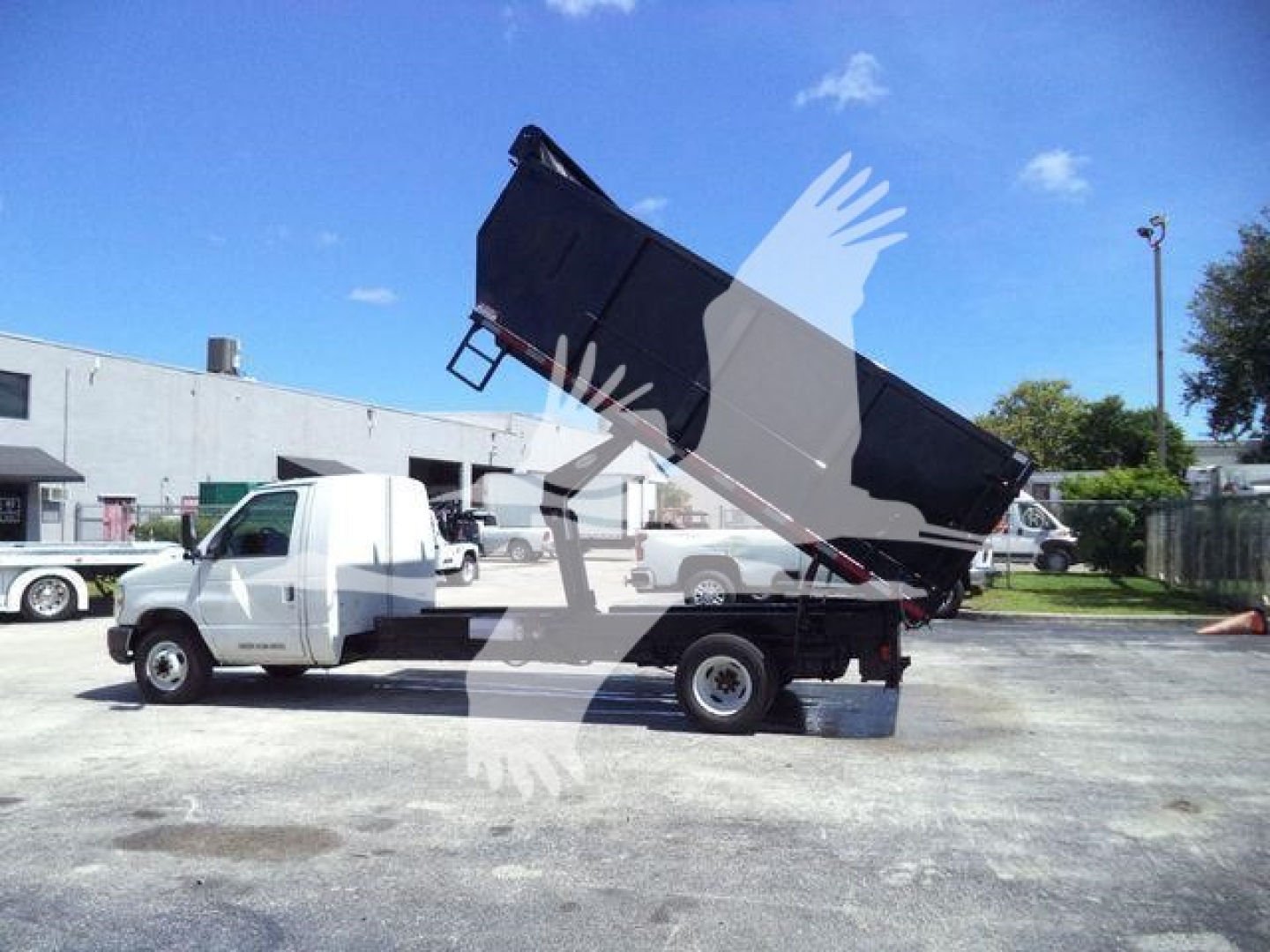 Ford E450 dump truck in-service showing raised dump bed on a light-duty chassis with white cab and black bed.