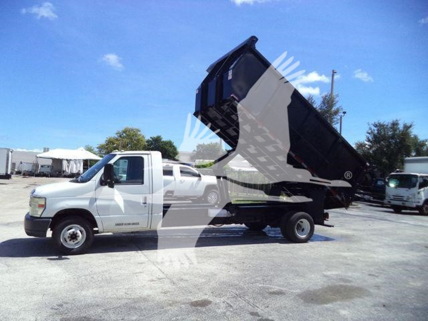 Ford E450 dump truck with bed raised, side view showing cab and dual rear wheels in a used trucks lot.