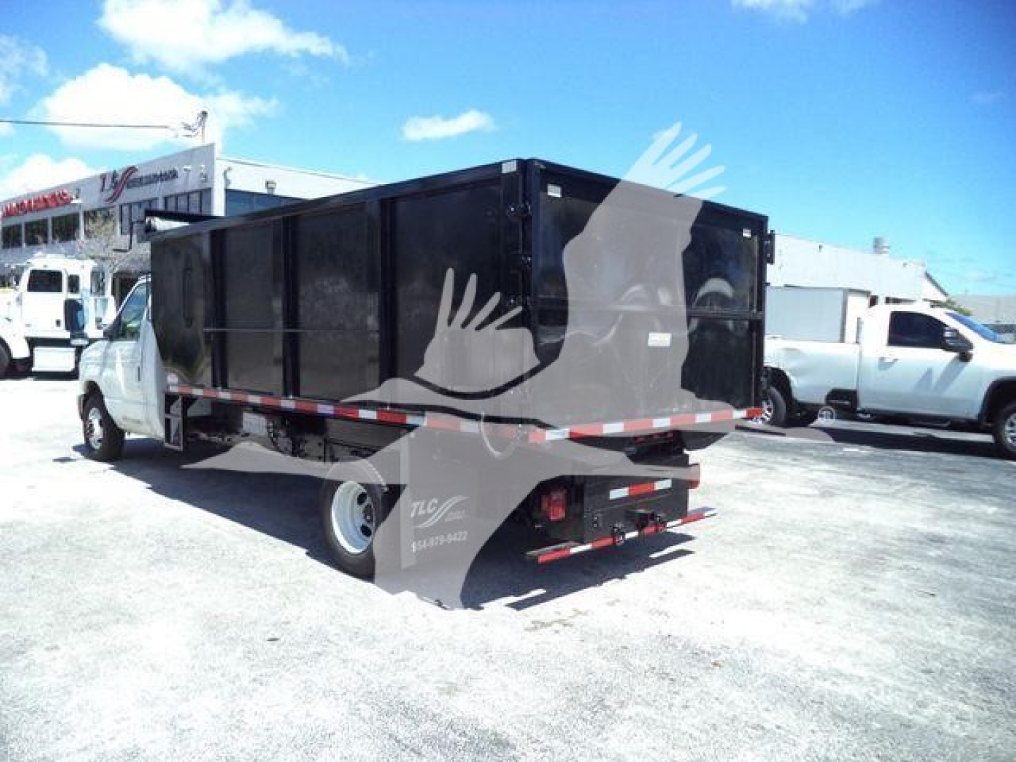 Dump truck chassis with a large black dump bed on a Ford E-450, rear view showing tailgate and hydraulic system access, in a dealership lot.