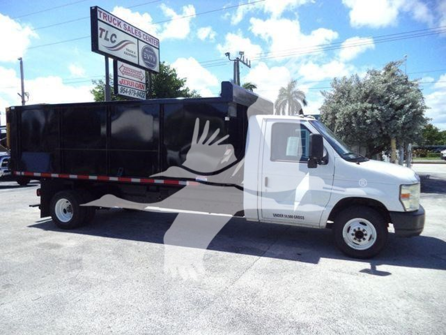 Ford E450 dump truck with black dump body and white cab, side graphic with a large hand logo, in a dealership lot.