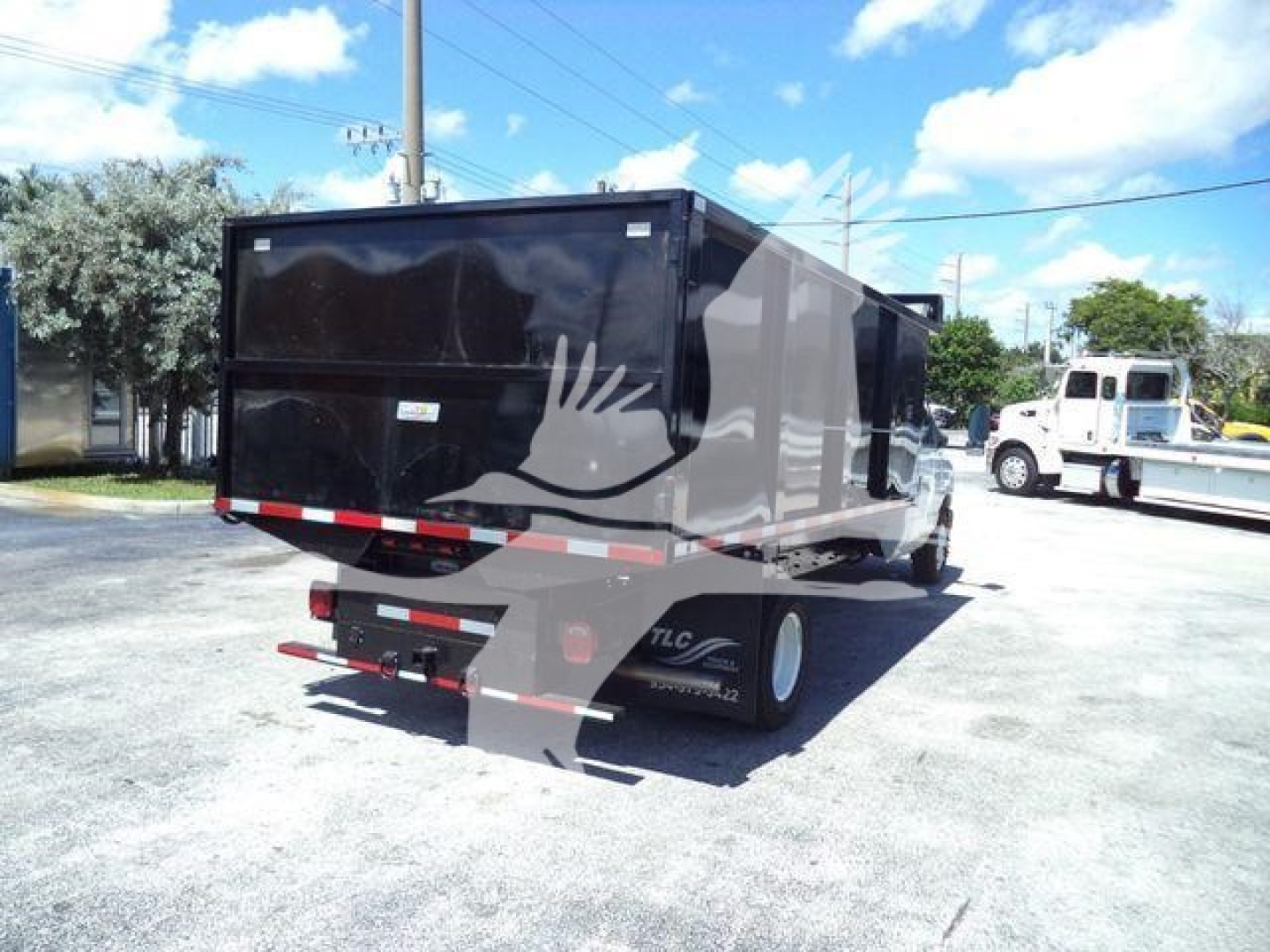 Black dump trailer attached to Ford E-450 chassis showing rear view with taillights and mud flaps.