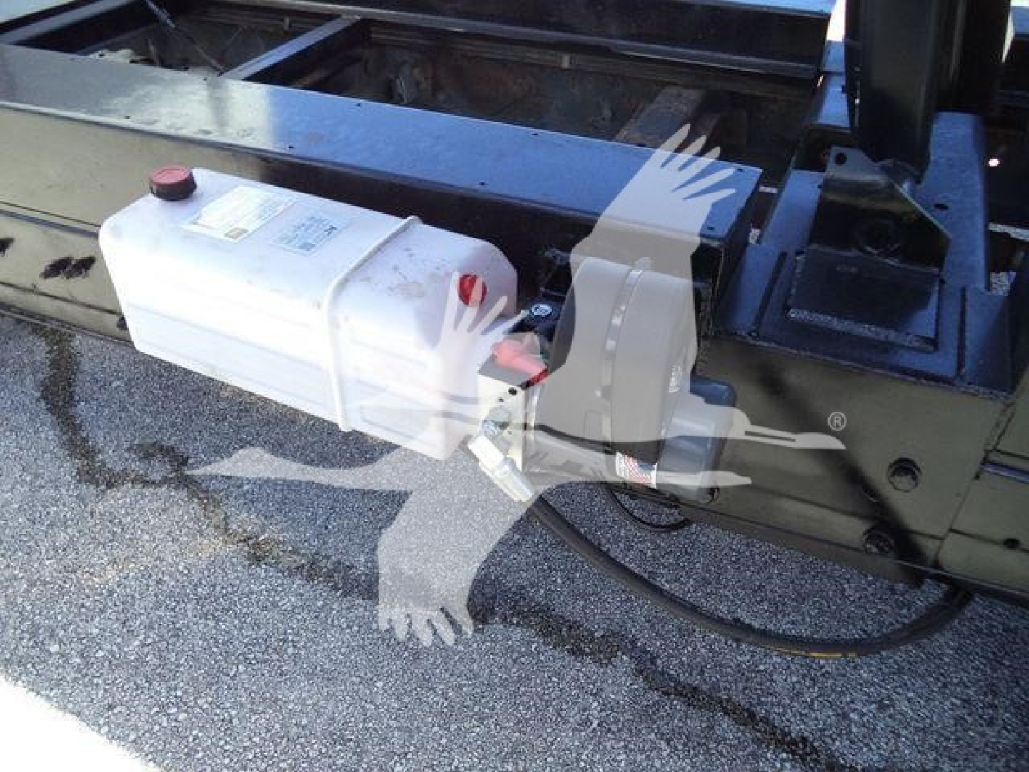 White plastic reservoir with red cap and hose attached mounted on a Ford E450 dump truck frame, visible chassis and hydraulic lines.
