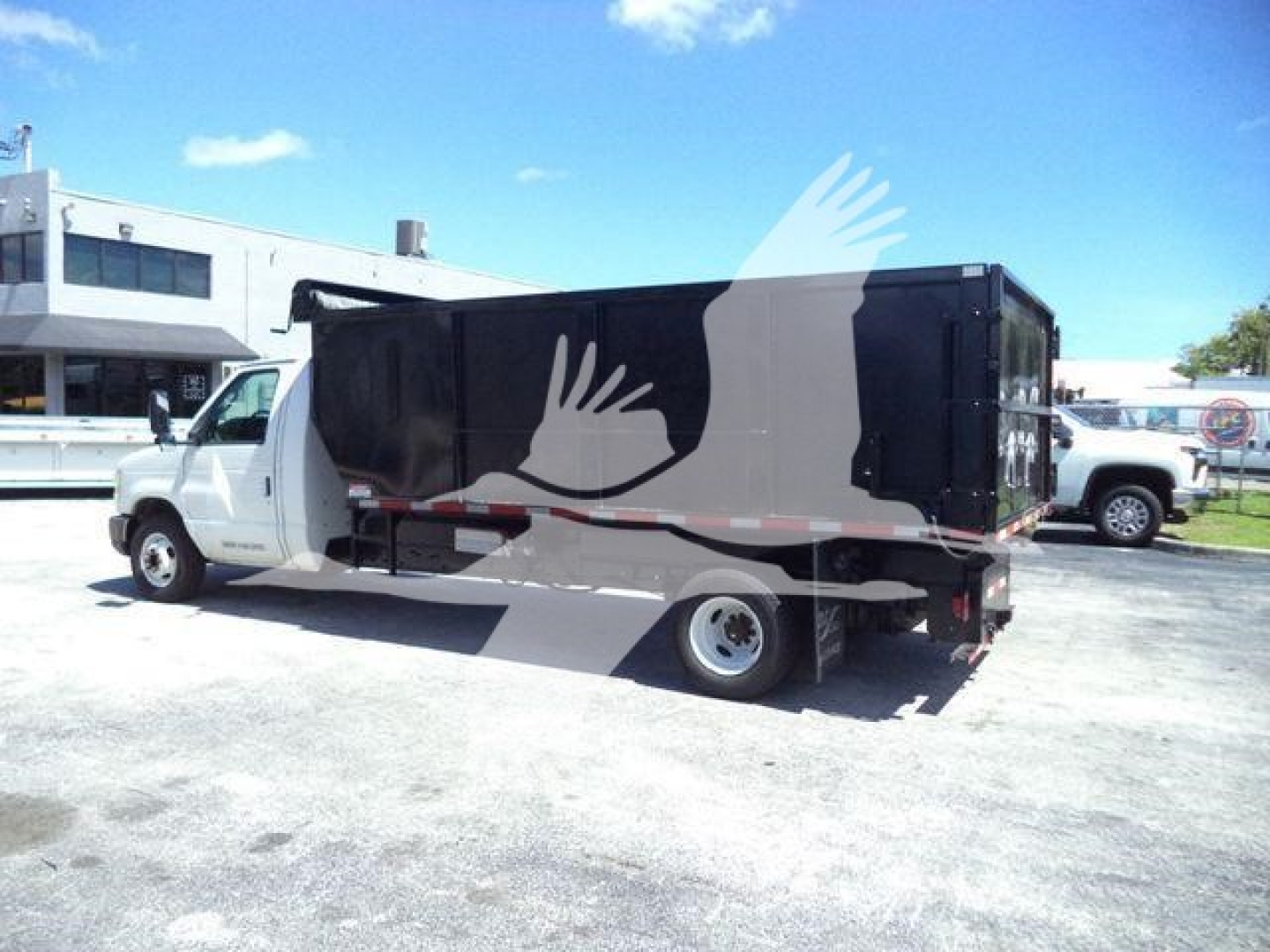 Ford E450 dump truck side view showing cargo box and cab with white body, black dump box, and rear tires; no visible text clearly legible.