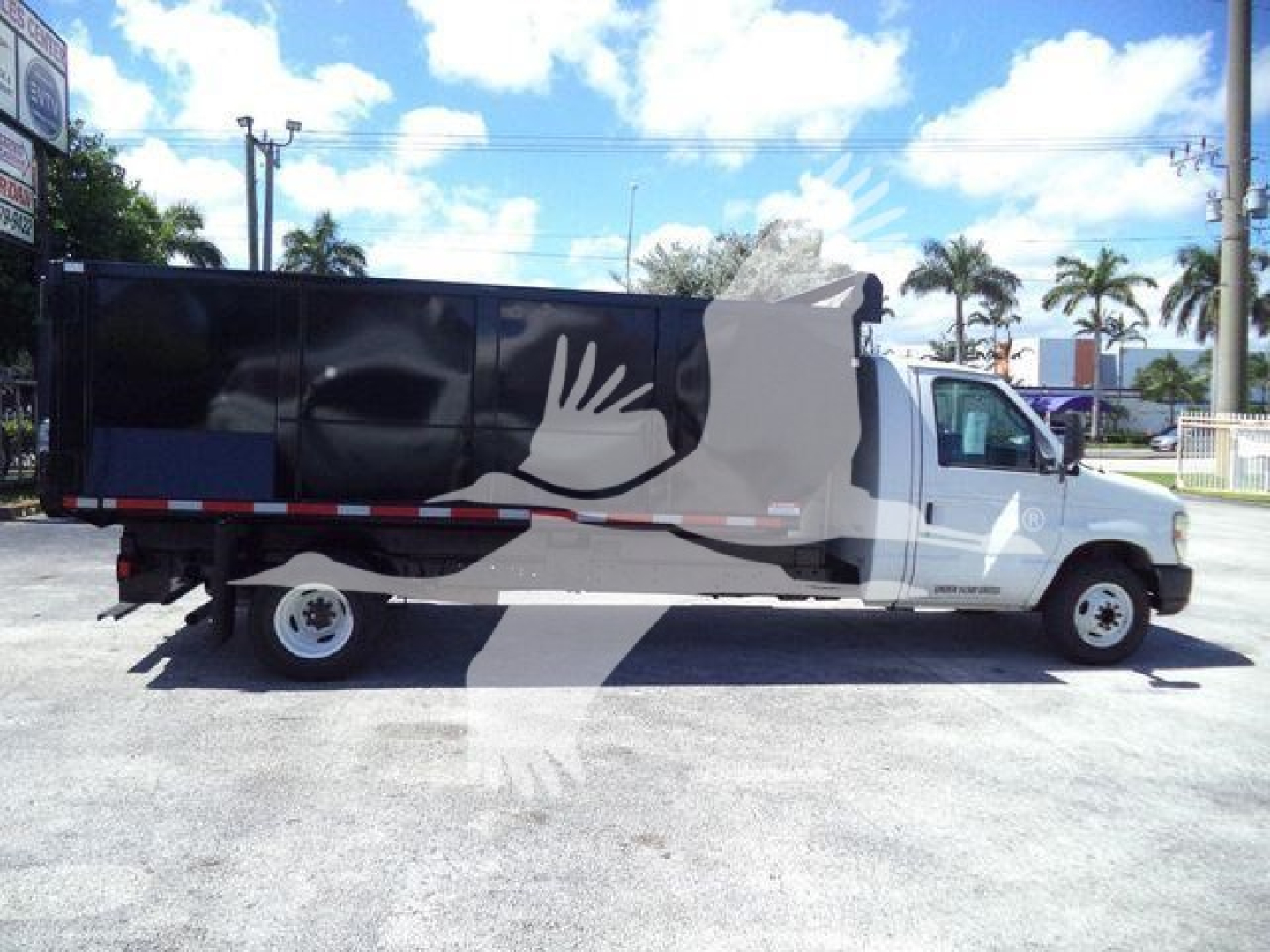 Ford E-450 dump truck side view showing black dump body with white graphic and gray cab, under clear sky.