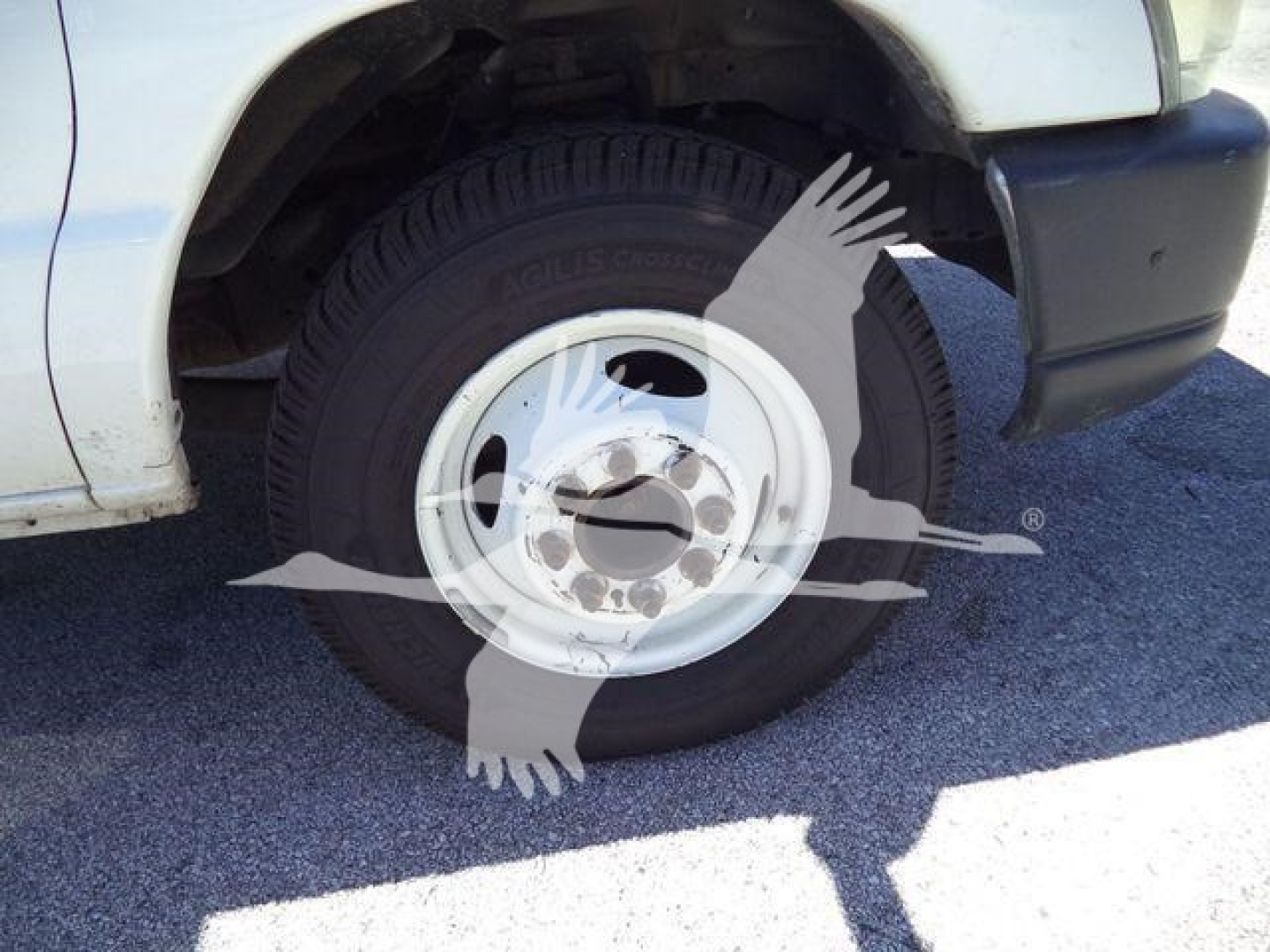 Front wheel of a white Ford E450 cargo/dump truck showing steel wheel and tire tread, fender and bumper visible.
