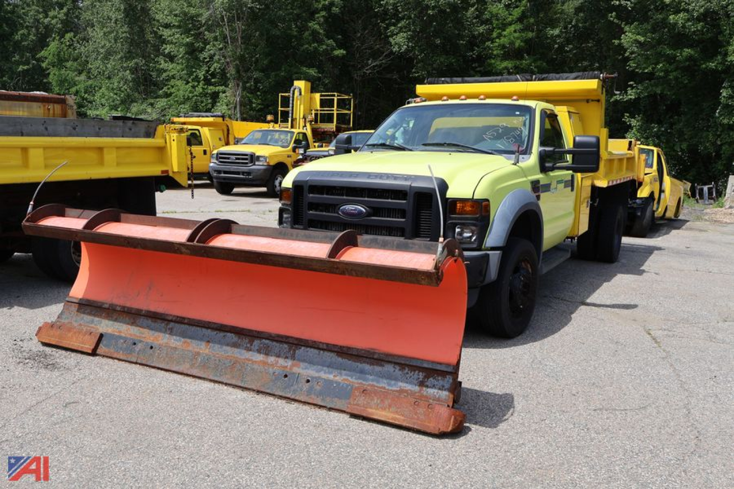 Ford F-450 Super Duty dump truck with large orange plow blade in front, yellow service trucks in background.