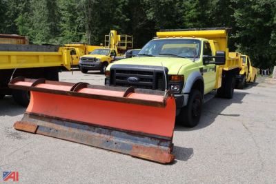 Ford F-450 Super Duty dump truck with large orange plow blade in front, yellow service trucks in background.