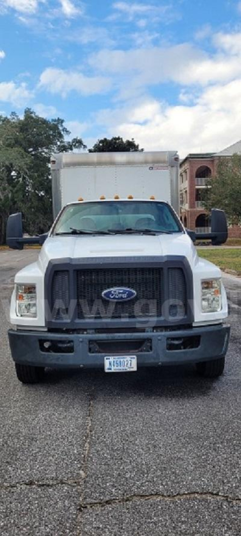 Ford F-650 front view showing grille, headlights, and bumper with Ford emblem, in-service white cab and truck box, license plate visible.