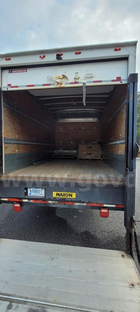 Open box truck rear with cargo area, Ford container. Interior shows wooden side walls, pallet, and rear lift; tailgate with Mayon/MAYON sticker and license plate area visible.