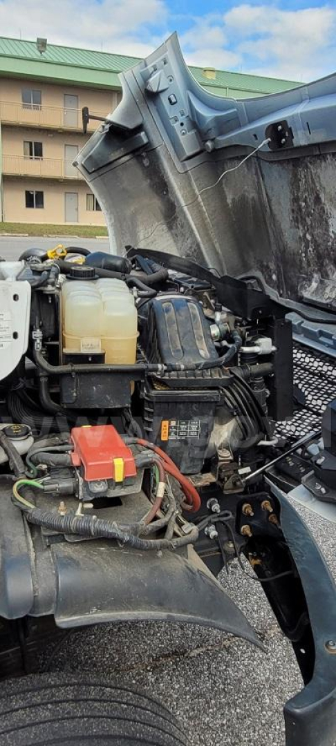 Ford F-650 engine bay with exposed hydraulic reservoir, battery, and wiring; truck hood open in parking lot.