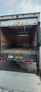 Open box truck rear with cargo area, Ford container. Interior shows wooden side walls, pallet, and rear lift; tailgate with Mayon/MAYON sticker and license plate area visible.