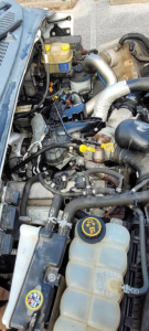 Ford F-650 engine bay showing coolant reservoir, yellow-capped fluid reservoirs, hoses, and turbo intercooler piping.