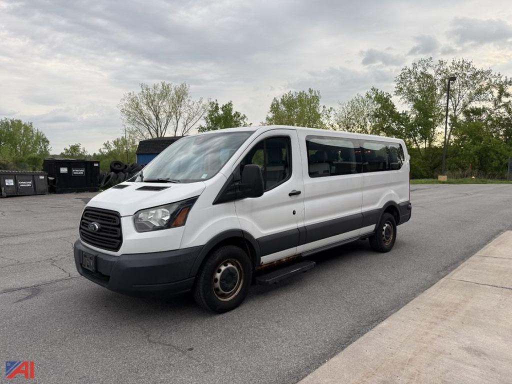 Ford Transit 2016 passenger van in light metallic color, front-left view, indicating cargo/passenger van with sliding side door and black bumpers.