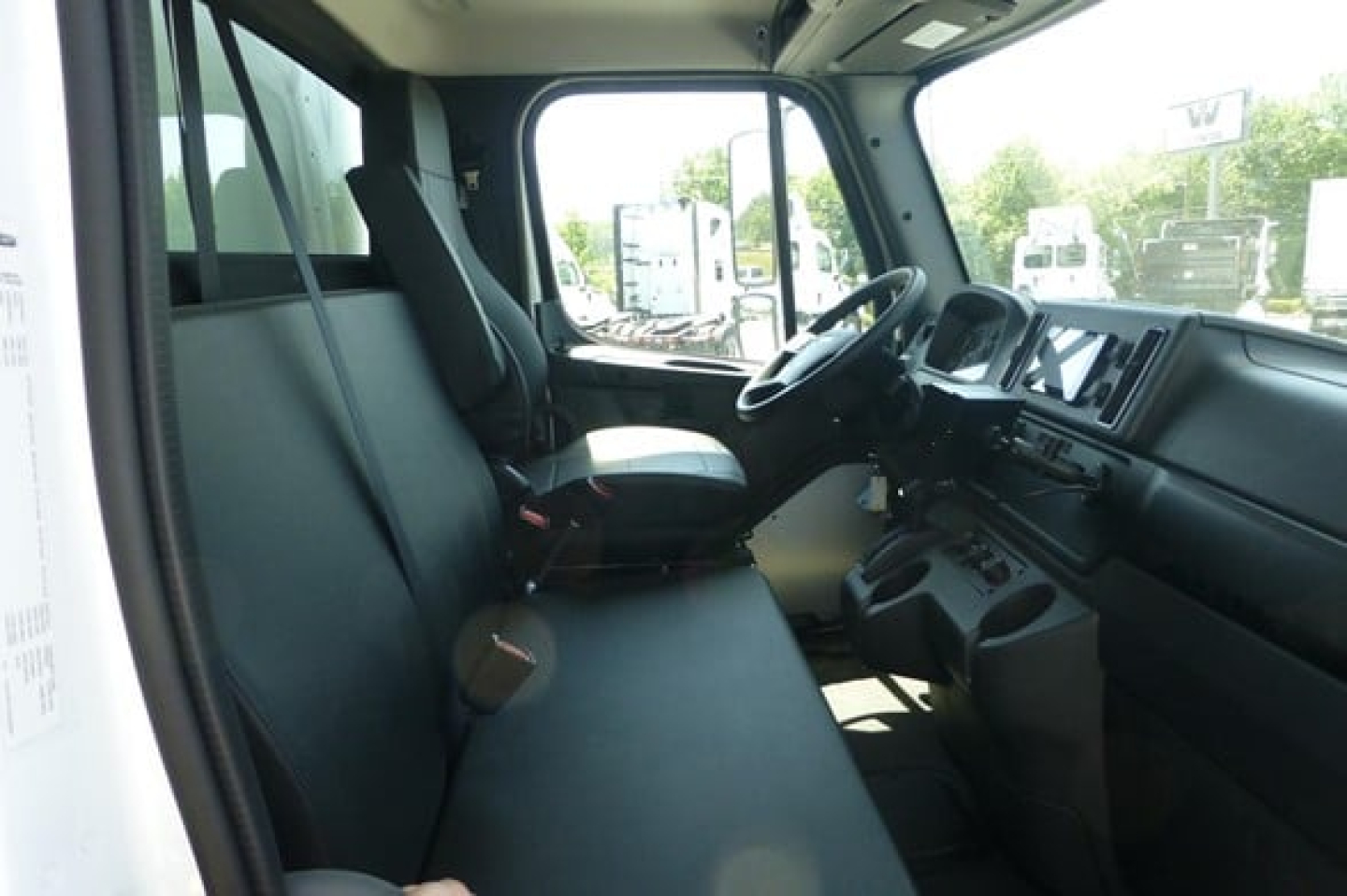 Cab interior of Freightliner M2 106 Plus showing front bench seat, steering wheel, dashboard, and driver area