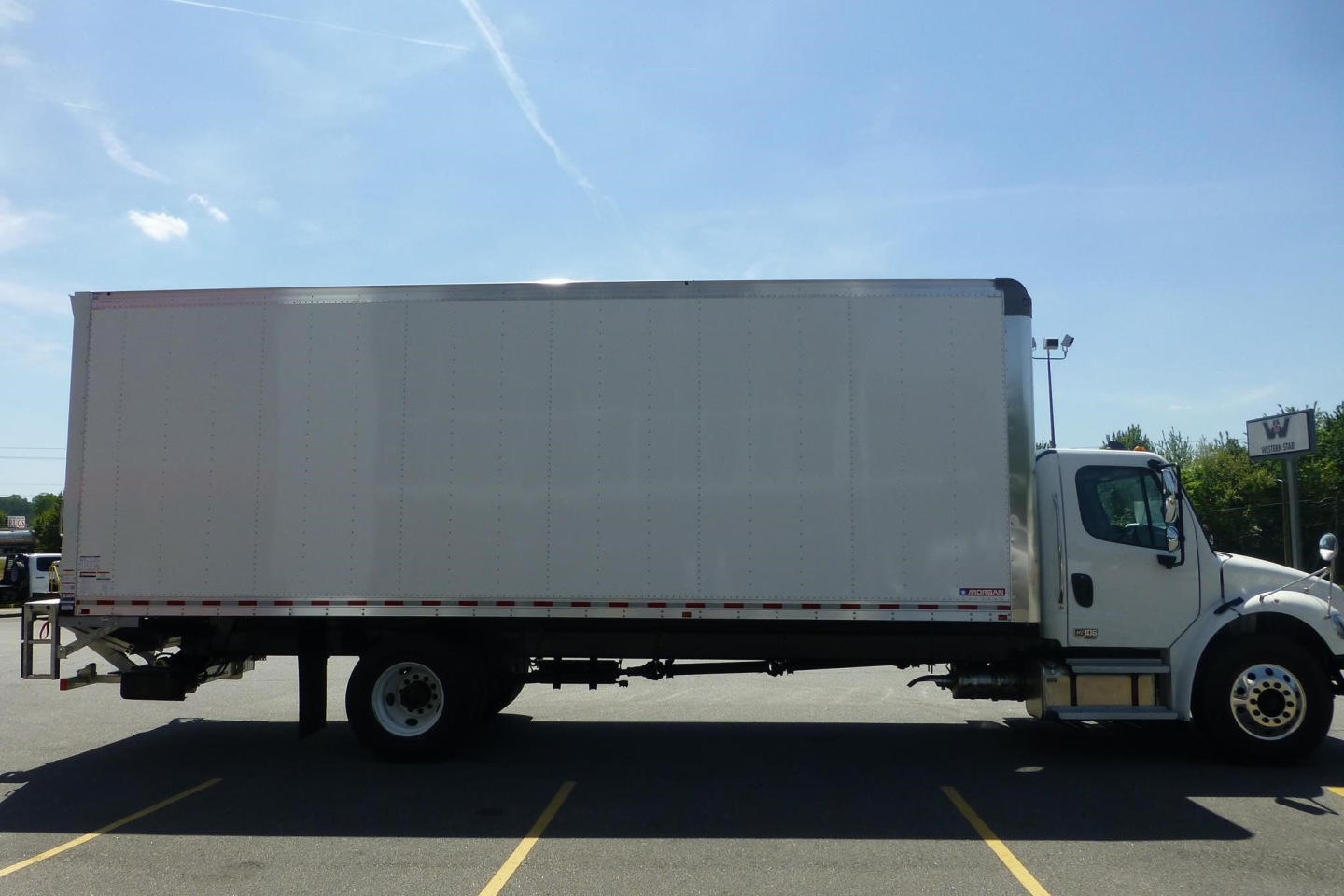 Side view of a Freightliner M2 106 Plus box truck with a white cab and large box body. No visible text on the truck body from this angle.