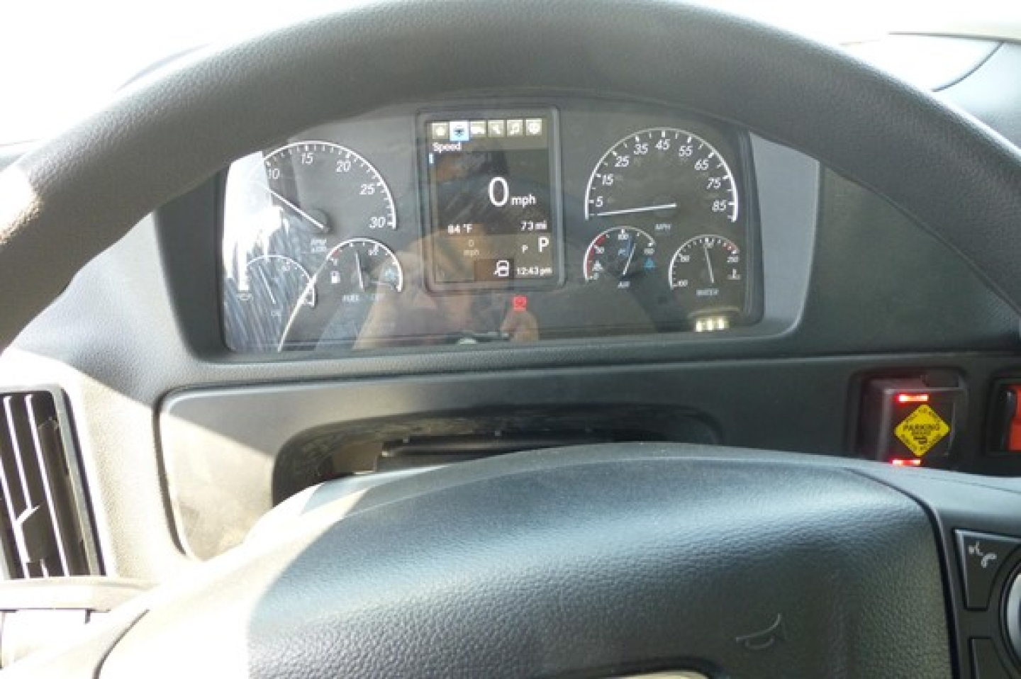 Dashboard view of Freightliner M2 106 Plus interior showing instrument cluster and steering wheel. Center display lit with 0 mph and various gauges.
