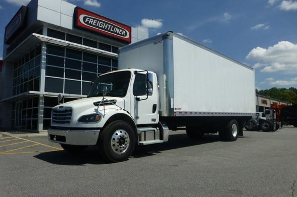  Freightliner M2 106 Plus box truck in dealership lot showing white cab and large rectangular cargo box.