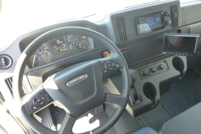 Cab interior of a Freightliner M2 106 Plus showing steering wheel, dashboard gauges, infotainment screen, and center console.