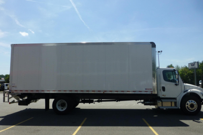 Side view of a Freightliner M2 106 Plus box truck with a white cab and large box body. No visible text on the truck body from this angle.