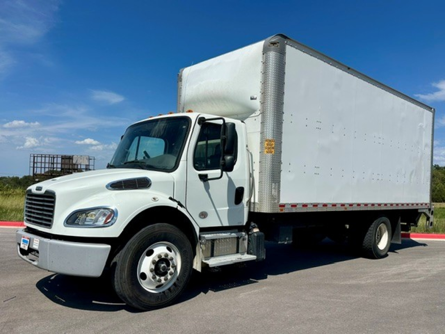 Box truck with white cab and large white cargo box, Freightliner M2-106, front wheel, side view showing cab and box.