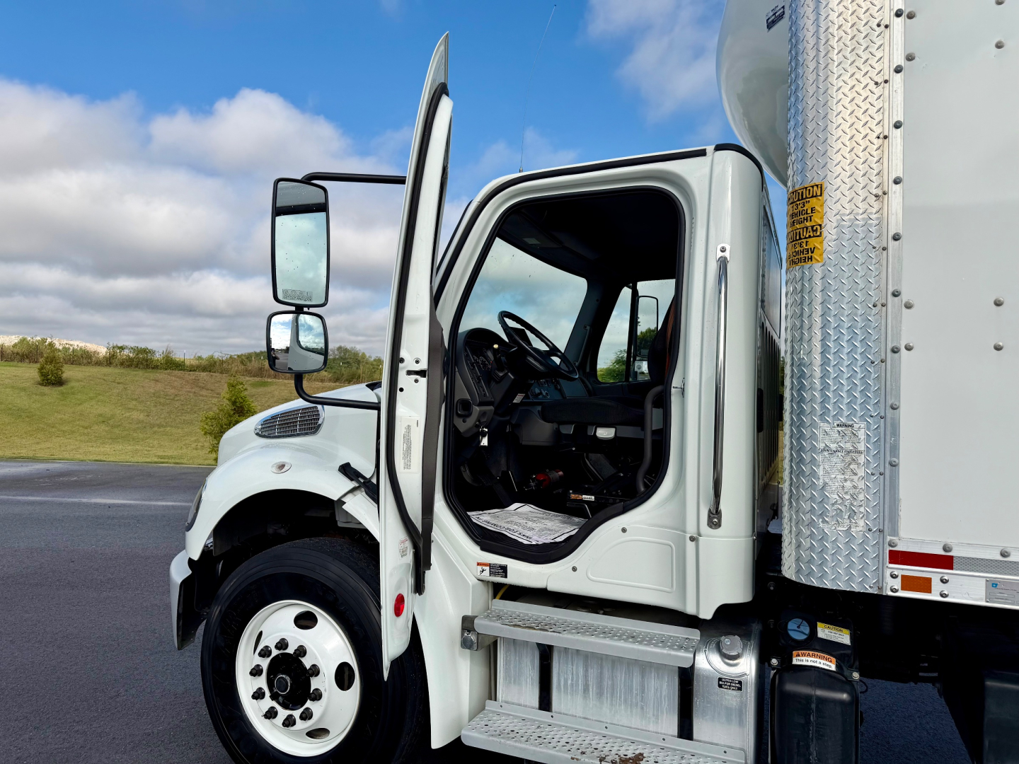 Freightliner M2-106 cab interior and open door showing steering wheel and dashboard with side cargo box.
