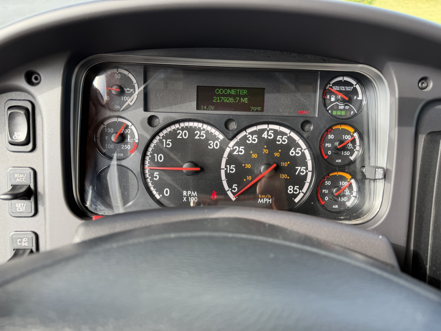 Dashboard view of a Freightliner M2-106 showing analog gauges, center digital display reading 21,700 miles and RPM gauge prominently in the middle.
