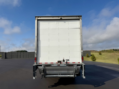 Freightliner M2-106 truck rear view showing roll-off-lift and box cargo area with white doors and bumper hardware.