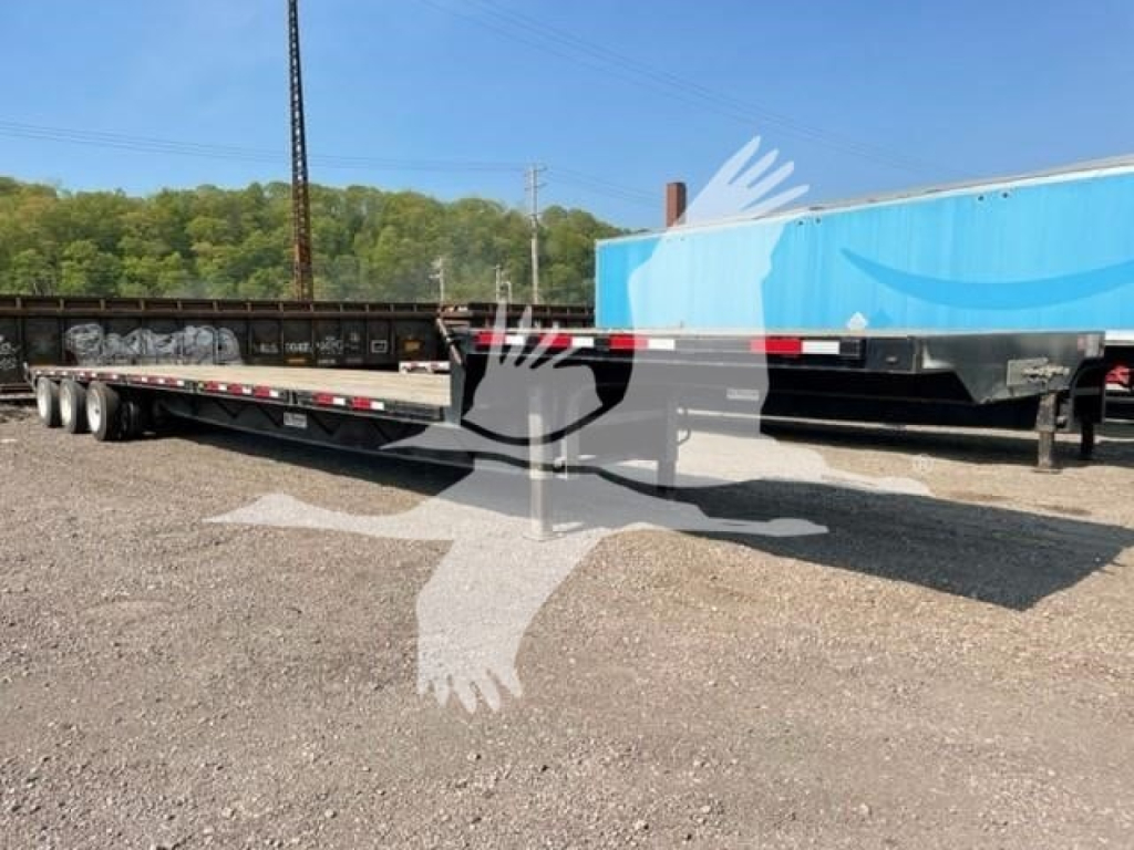 Transcraft drop deck trailer showing long flatbed with multiple axles and reflective tape along sides.