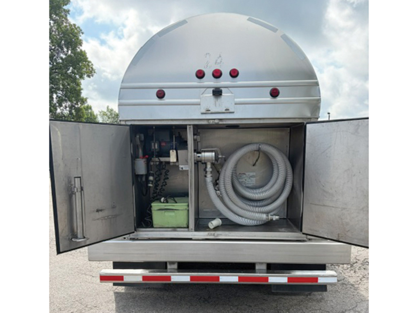 Tank trailer rear with open compartments showing hose reel and a green battery/power unit inside, Brenner STPU60001ISS trailer model.