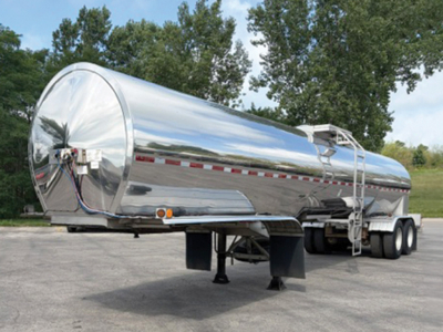 Flatbed trailer tank with polished aluminum cylindrical tank and dual rear axles, landing legs down, VIN XMOM2210 visible on listing.