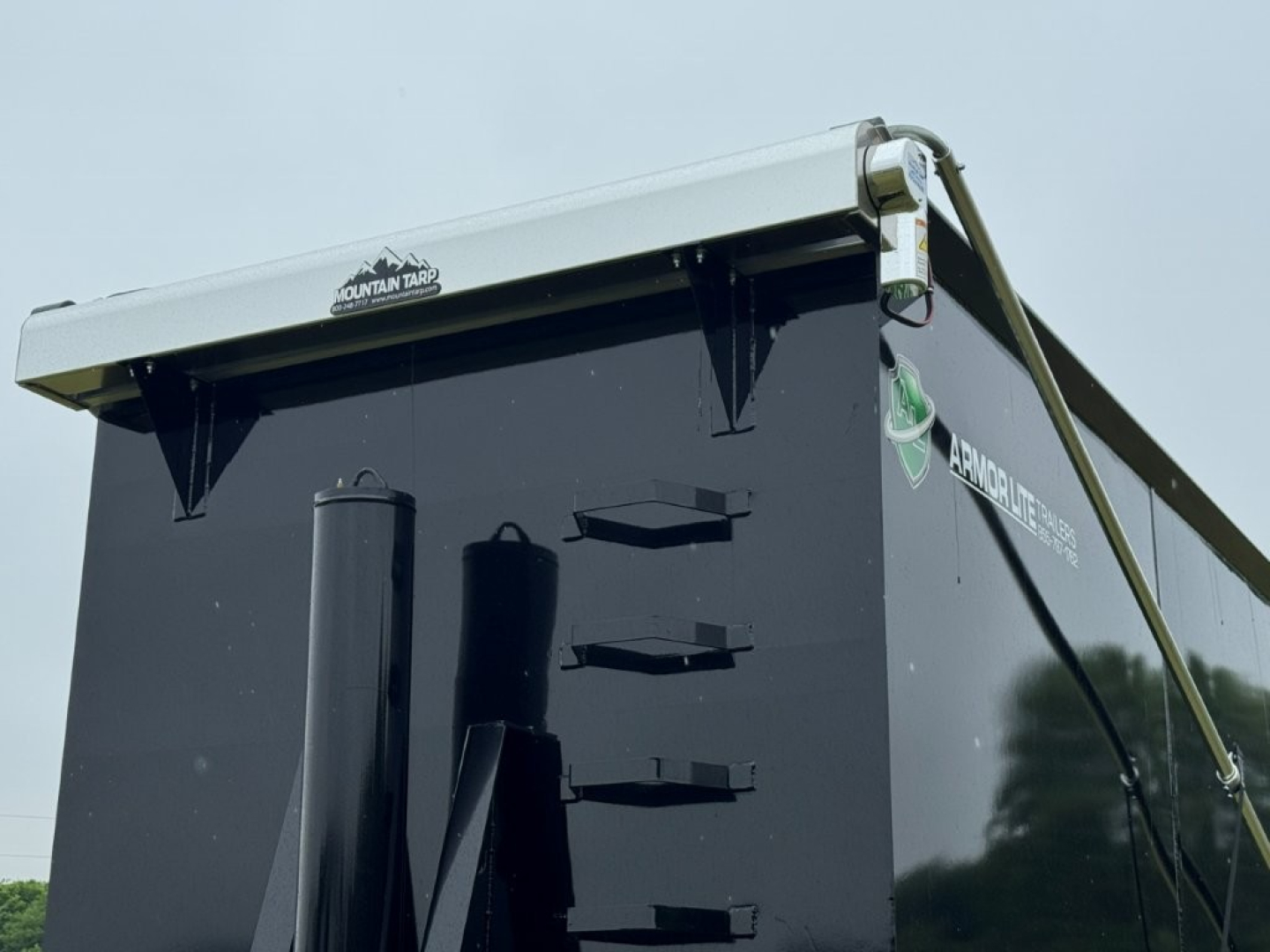 Dump trailer showing vertical side access hatches, black body with white top rail, Montana tarp logo on side and rear.