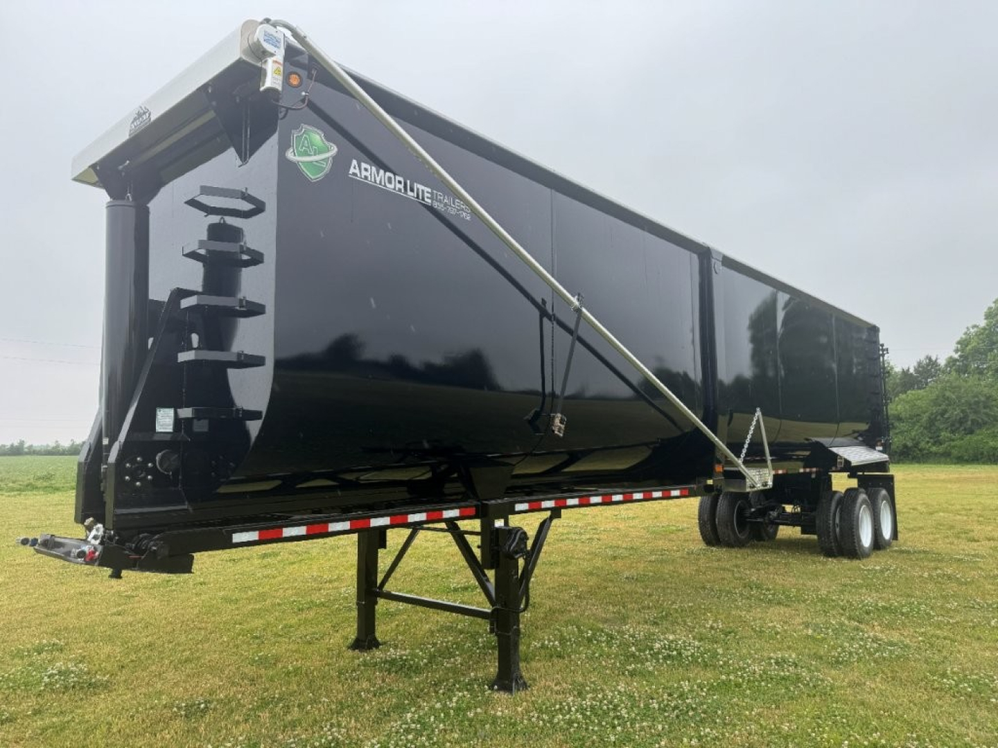 Armor Lite trailer showing 40' x 100" dump trailer with black sides, front landing gear, and tandem axle on a gravel field.