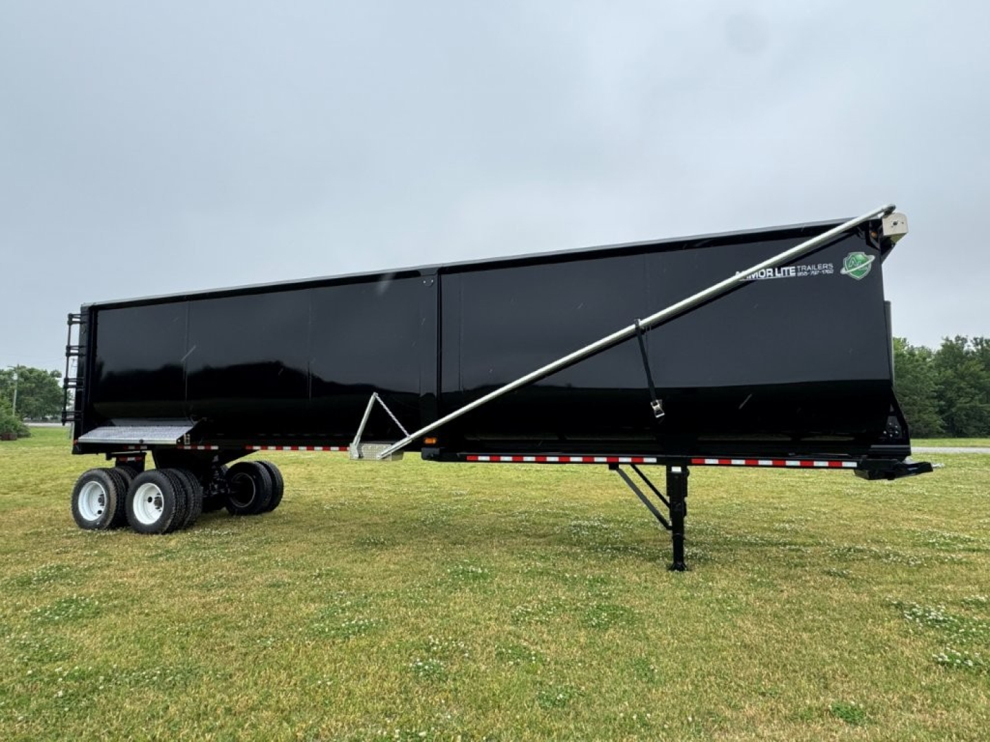 Armor Lite dump trailer with side panel and landing gear visible. Text on side reads Armor Lite; rear area shows support jack and wheels.