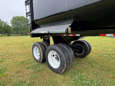 Trailer underside view showing dual rear axles and black dump trailer with white wheels and diamond plate step.